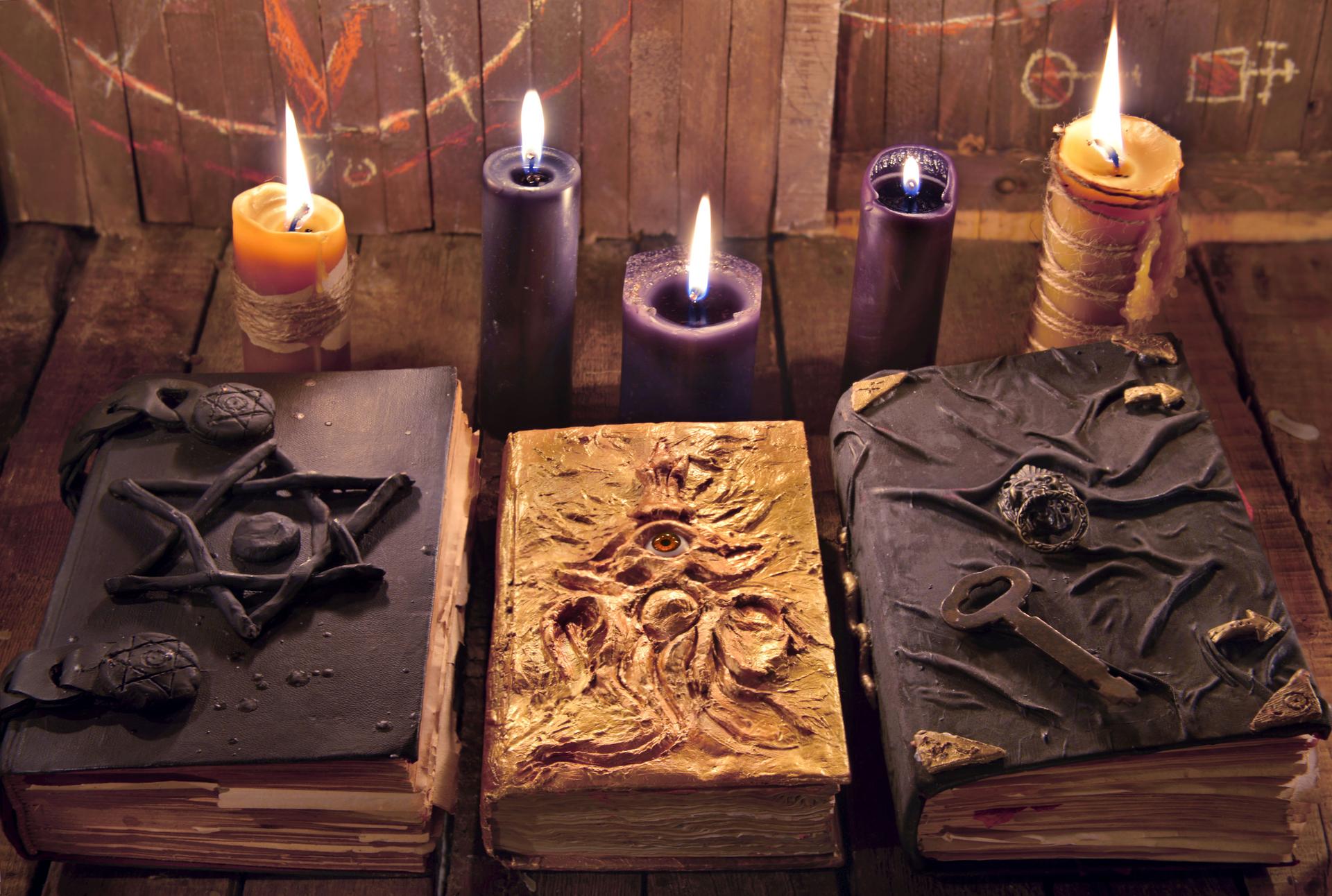 Three magic books with burning candles on planks