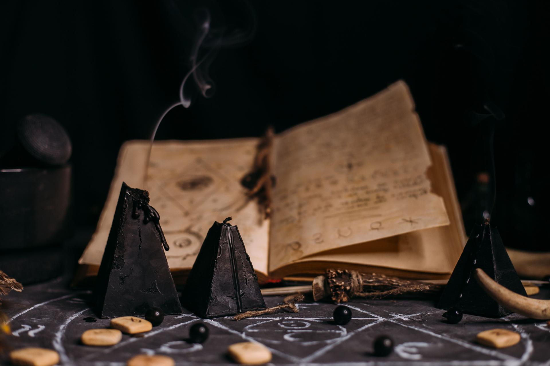 Open old book with magic spells, runes, black candles on witch table. Occult, esoteric, divination and wicca concept.