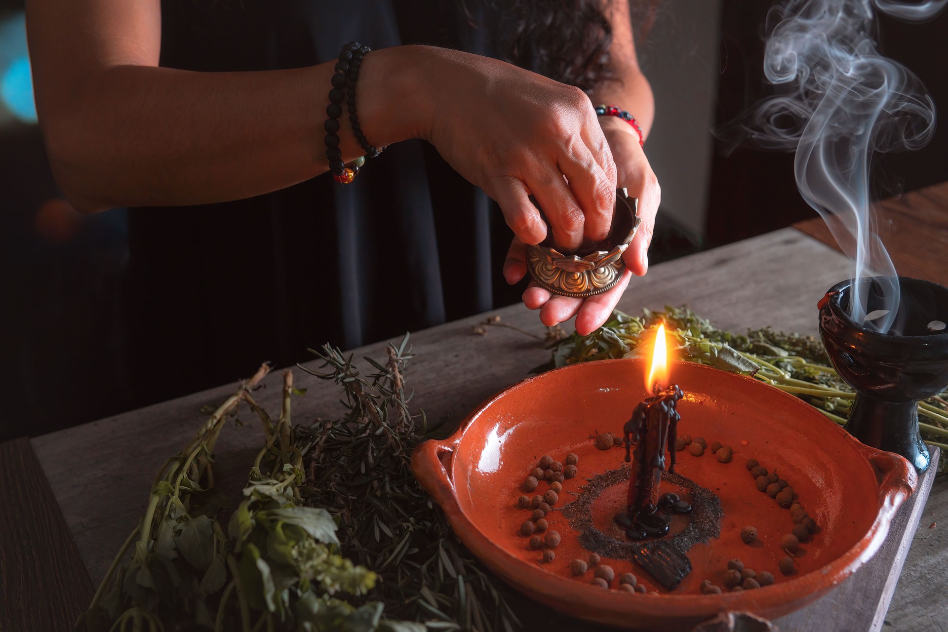woman doing traditional ritual with black candle sea salt pepper in clay plate with herbs and incense and energy management with fire